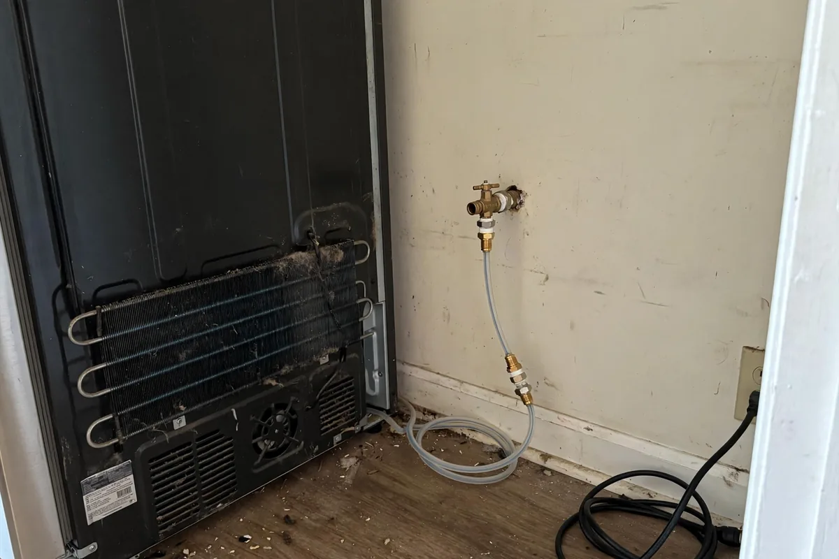 Refrigerator pulled out revealing the ice maker water supply line and its connections at the back