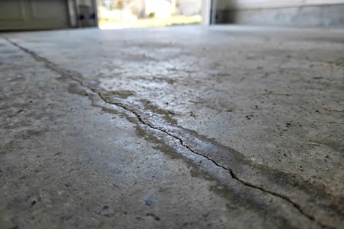 Hairline crack with damp discoloration running across a concrete garage floor